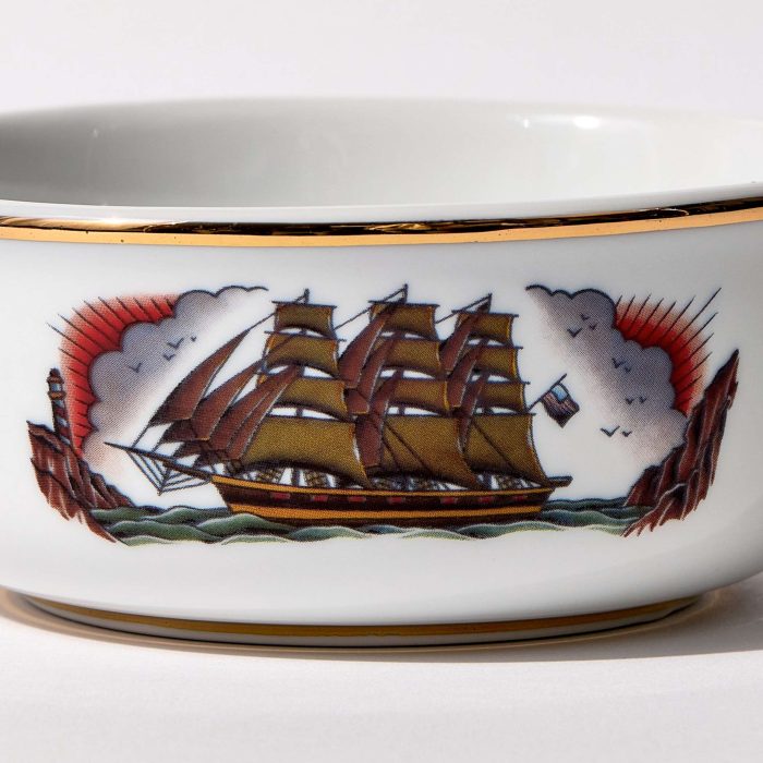 Detail view of porcelain shaving bowl with illustration of vintage sailing ship and port backdrop, gold trim