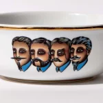 Detail view of porcelain shaving bowl with illustration of Victorian-era gentlemen portraits, gold trim