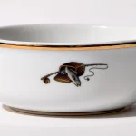 Detail view of back of shaving bowl with illustration of vintage fishing creel, fish, rod, and reel, gold trim