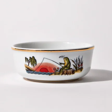 Porcelain shaving bowl with illustration of anthropomorphic frog fishing and riverside backdrop, gold trim