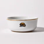 Back of shaving bowl with illustration of vintage motorcycle cap, gloves, goggles, and checkered flag, gold trim