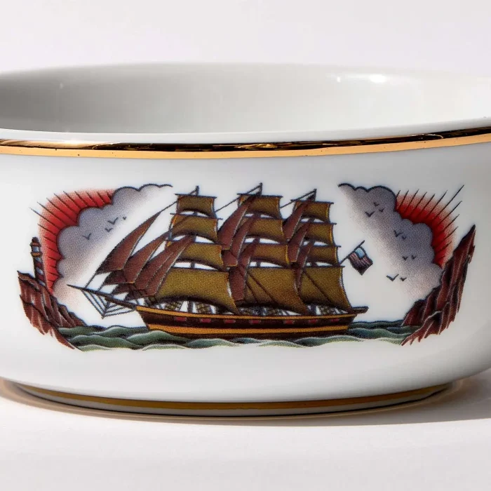 Detail view of porcelain shaving bowl with illustration of vintage sailing ship and port backdrop, gold trim