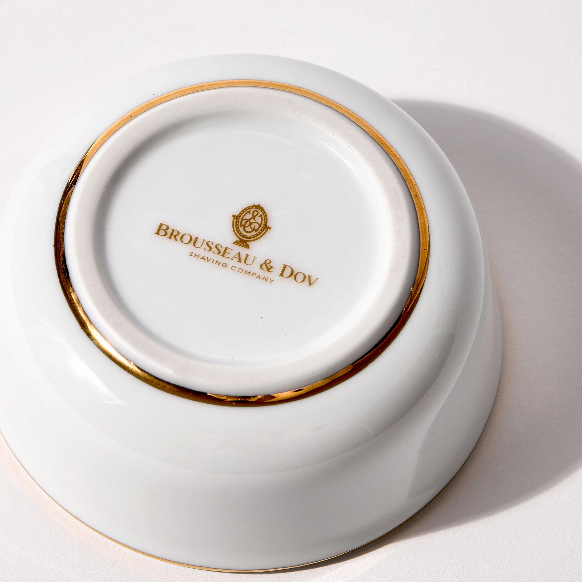Bottom of porcelain shaving bowl showing gold Brousseau & Dov logo, gold trim, and foot